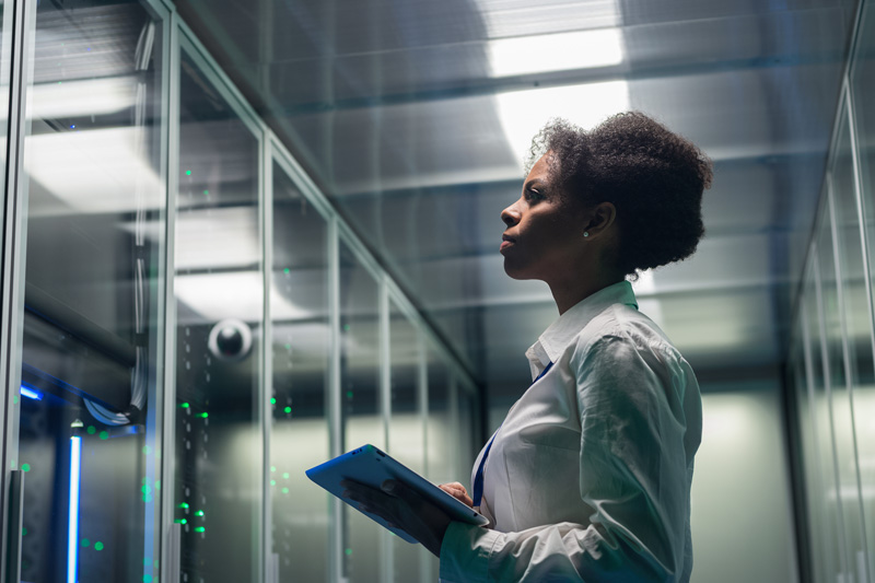 female technician working on a tablet in a data center full of rack servers running diagnostics and maintenance on the system
