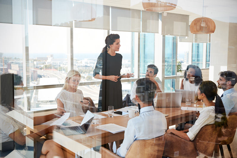 Businesswoman Leads Meeting Around Table Shot Through Door